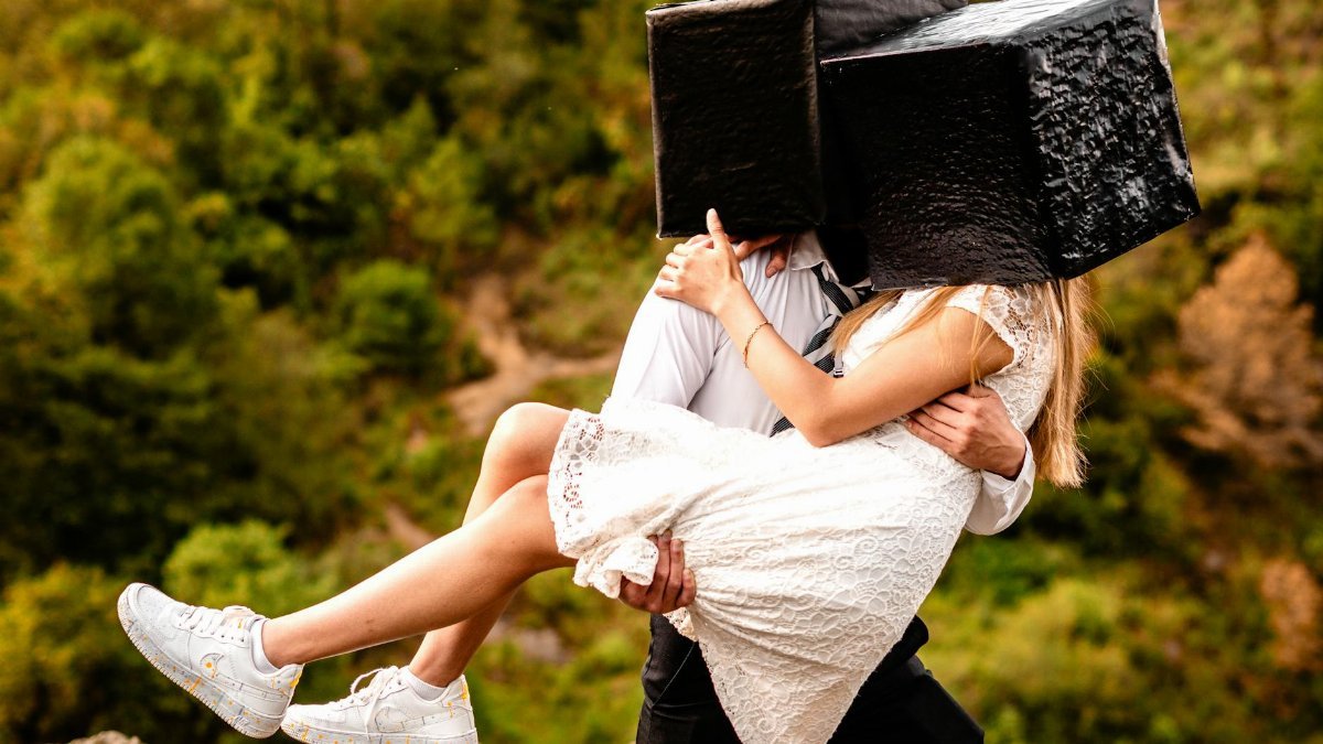 Couple embracing outdoors with unique black box headwear, showcasing creativity in nature.