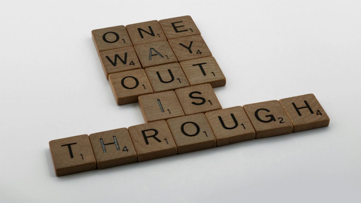 Close-up of Scrabble tiles spelling 'one way out is through' on a white surface.