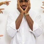 Worried man surrounded by pointing fingers, symbolizing bullying and social pressure.
