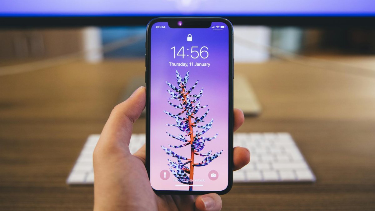 Close-up of a hand holding a smartphone with a vibrant purple screen displaying the time and date.