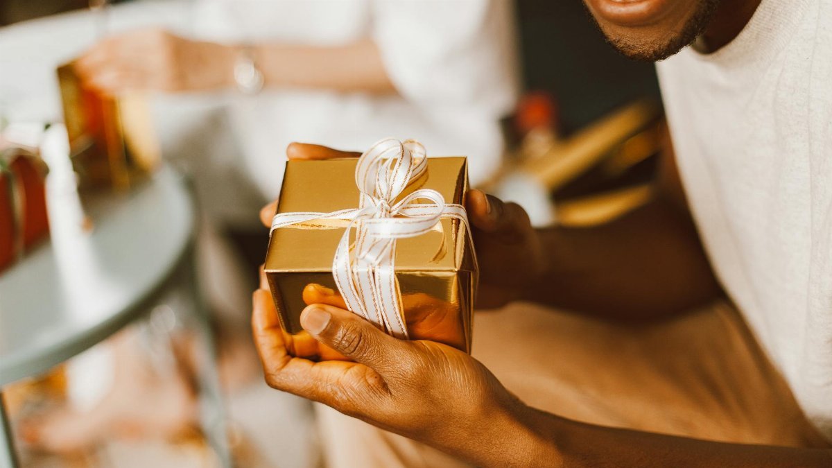 Close-up of hands holding a gold gift box with a ribbon, capturing a joyful indoor moment.