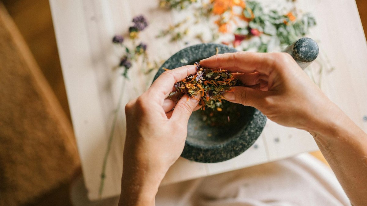 Close-up of hands mixing dried herbs with a mortar and pestle for herbal medicine preparation.