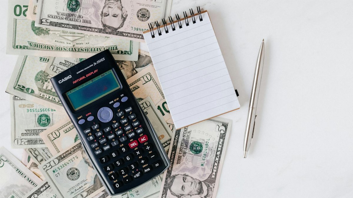 Flat lay of US dollar bills with calculator and notebook for budgeting.