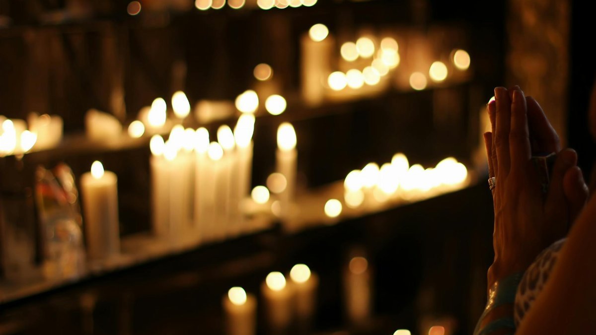 Hands clasped in prayer by candlelight in a church in São Paulo, Brazil, evoking a spiritual atmosphere.