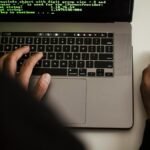Close-up of a programmer typing on a laptop, displaying code on the screen.