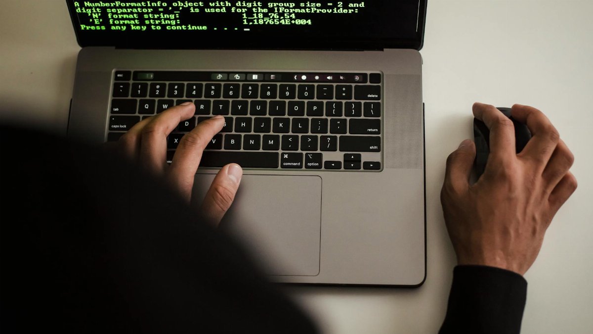 Close-up of a programmer typing on a laptop, displaying code on the screen.