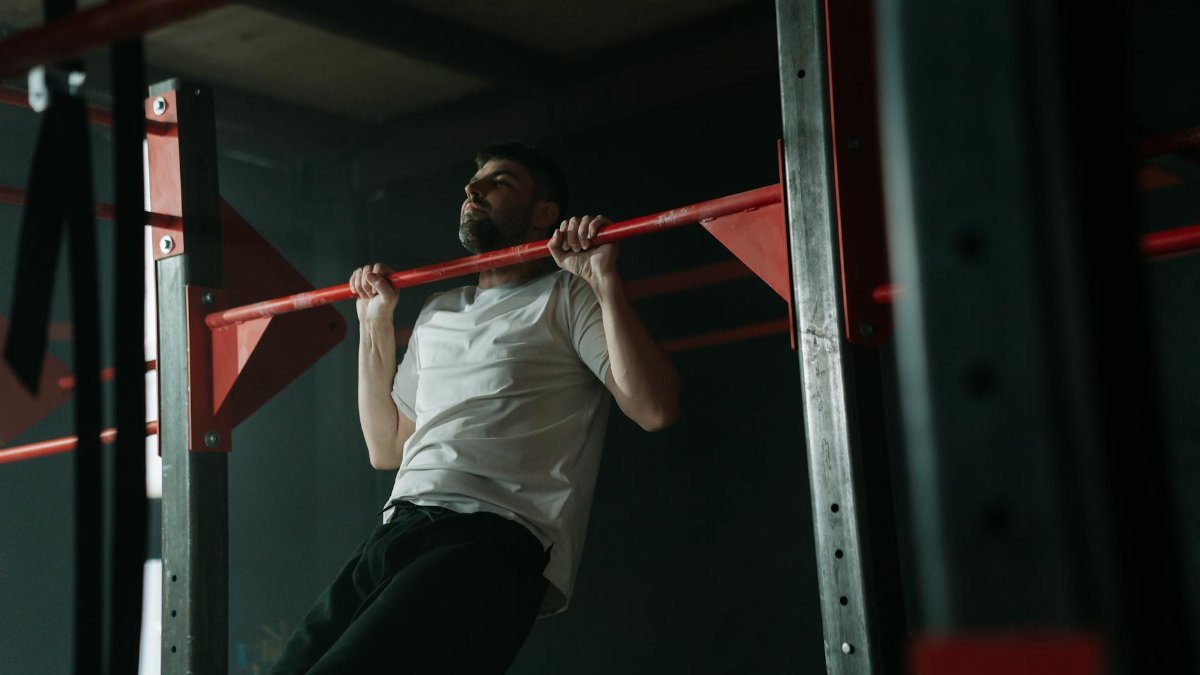 Adult male doing pull-ups on a red gym bar, symbolizing strength and fitness.