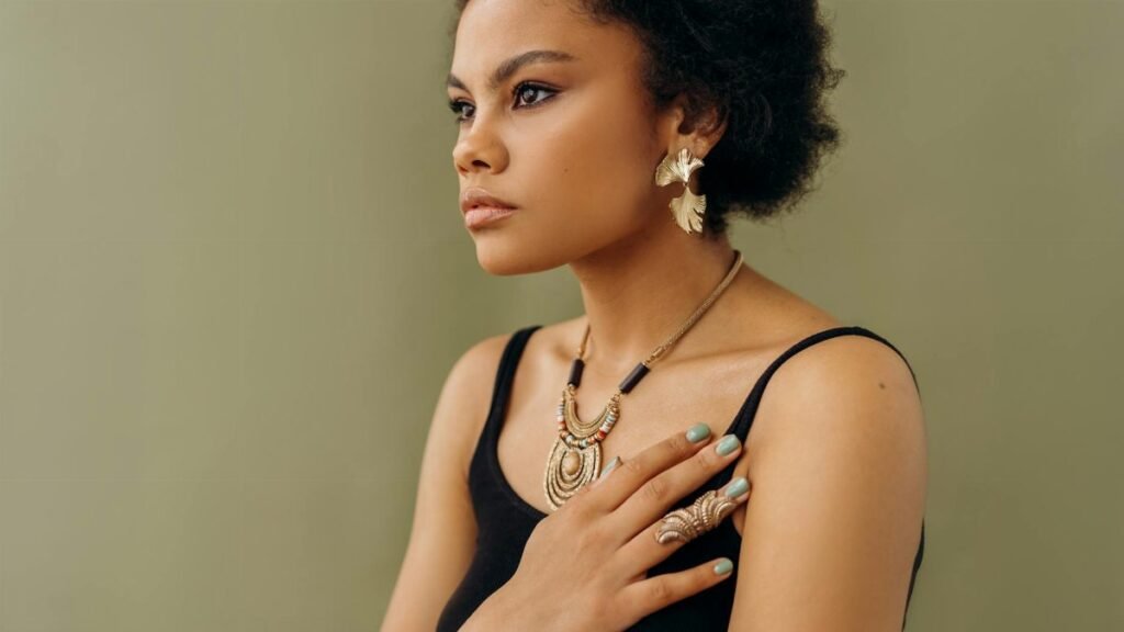 A stylish woman in elegant jewelry poses against a neutral background, exuding confidence.