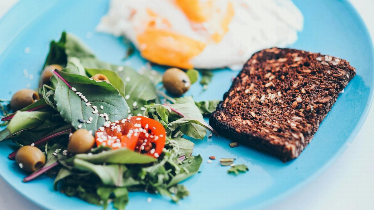 A nutritious breakfast plate featuring eggs, rye bread, salad, and olives on a vibrant blue plate.