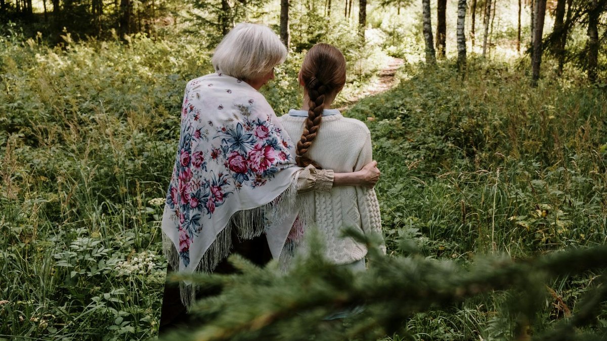 Grandmother and granddaughter walking in a forest, sharing a moment of connection and nature.