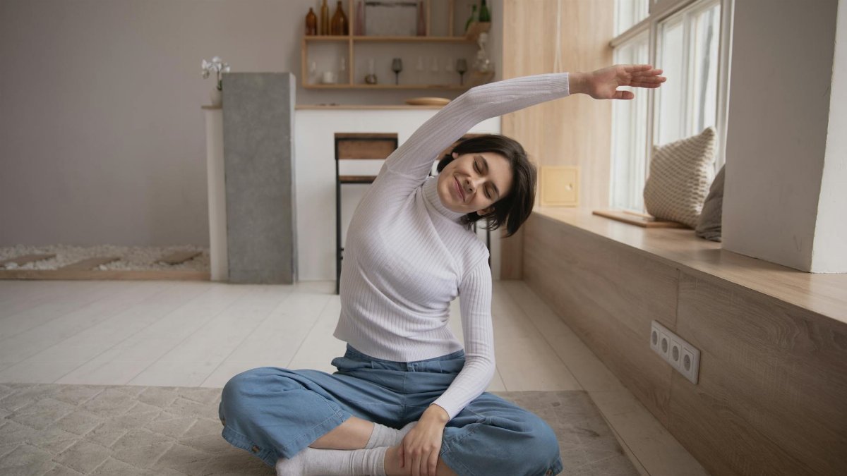 A young woman sitting in a peaceful home, stretching while practicing yoga for relaxation.