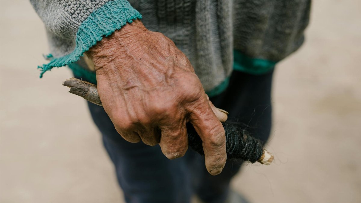 Detailed view of an elderly man's hand holding a tool, showcasing aged skin and textile texture.