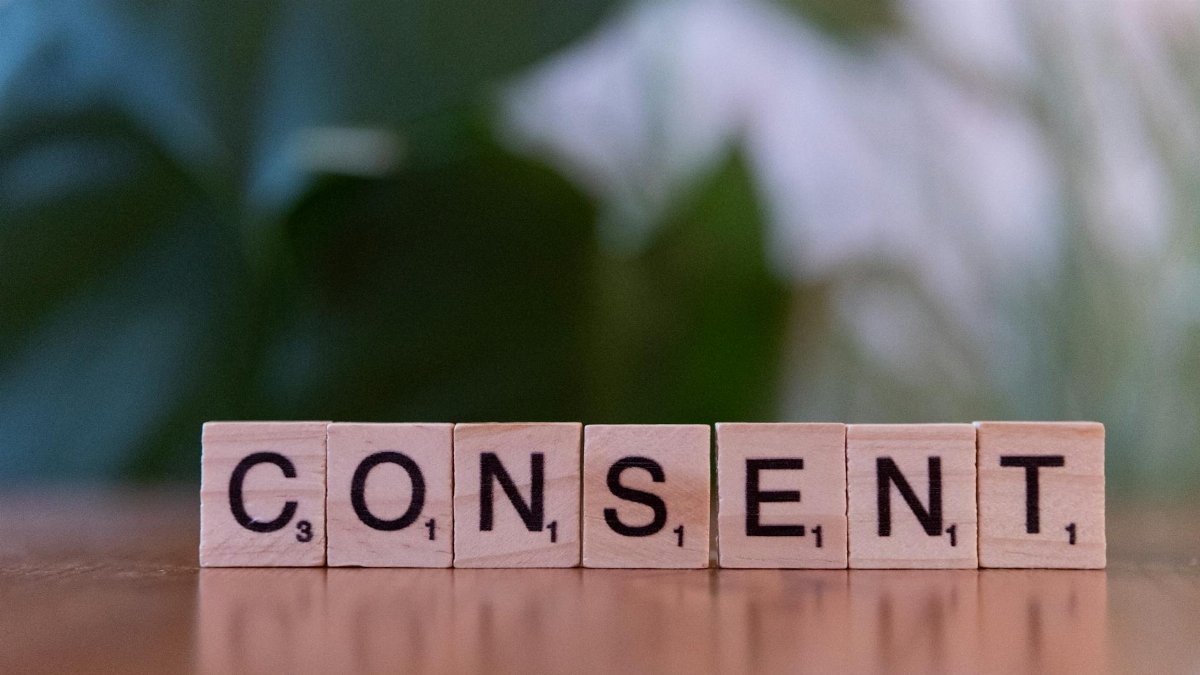 Close-up of Scrabble tiles spelling 'Consent' on a wooden surface, focusing on ethics and communication.