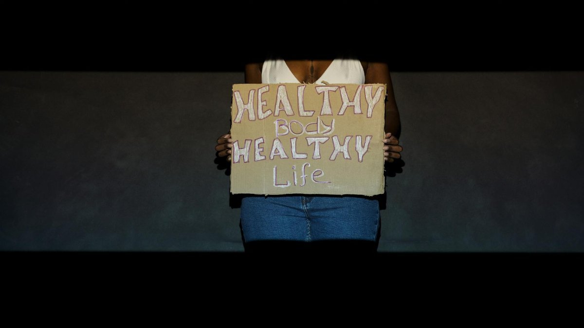 Person holding a cardboard sign with 'Healthy Body, Healthy Life' message in dim light.