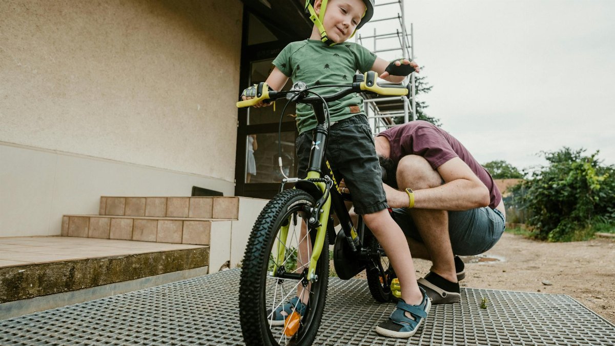 Father assisting young son with bicycle in backyard, teaching safe riding.