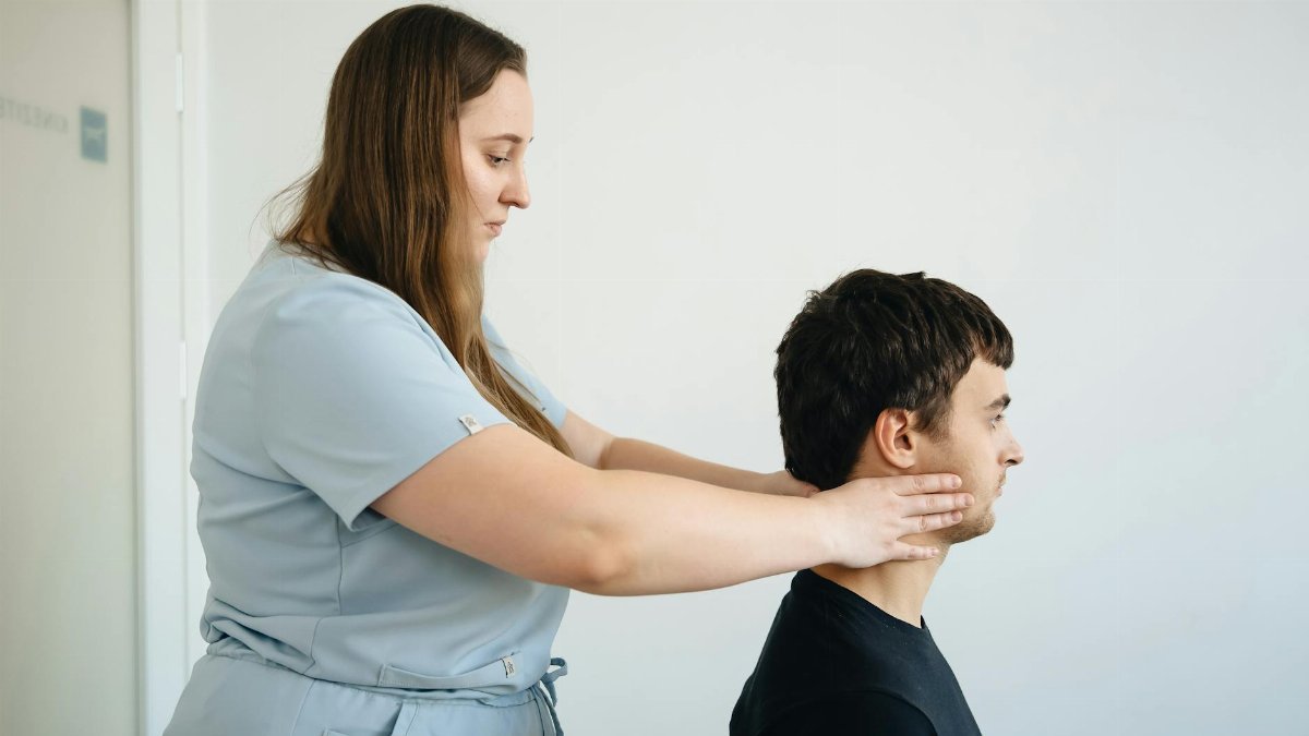 A physiotherapist performs a neck adjustment on a male patient in a clinic setting.