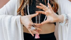 A woman wearing jewelry holds a clear healing crystal, symbolizing spiritual wellness.