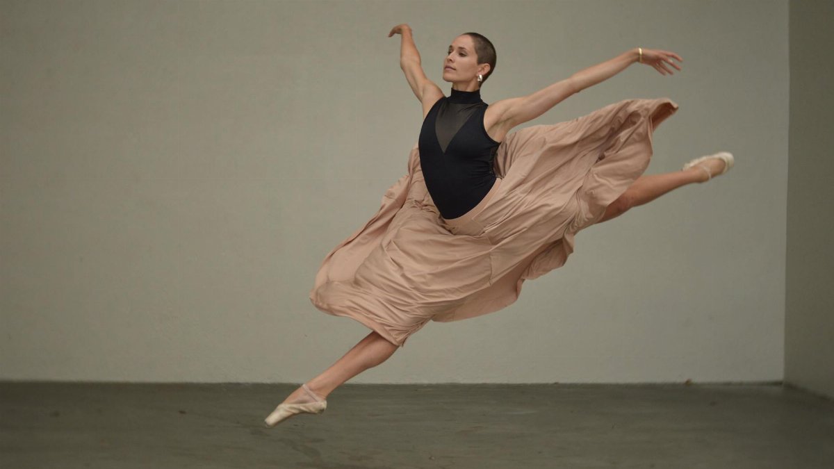 A skilled ballerina showcases grace in a poised, full-length leap indoors.