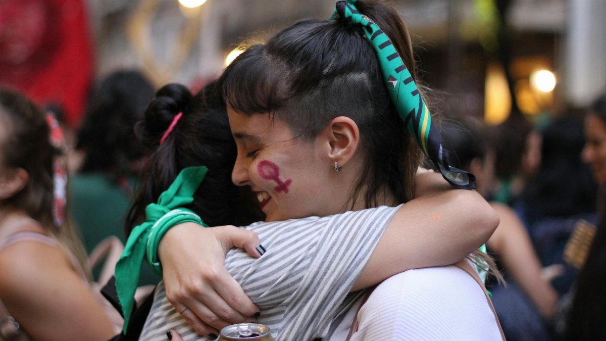 Two women hugging with face paint in a lively outdoor celebration, conveying unity and friendship.