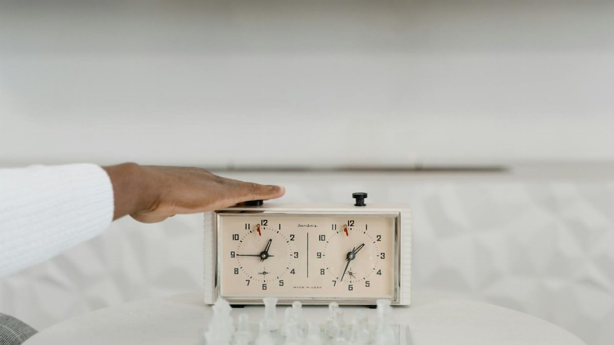 A classic chess clock being pressed by a player during a strategic game indoors.