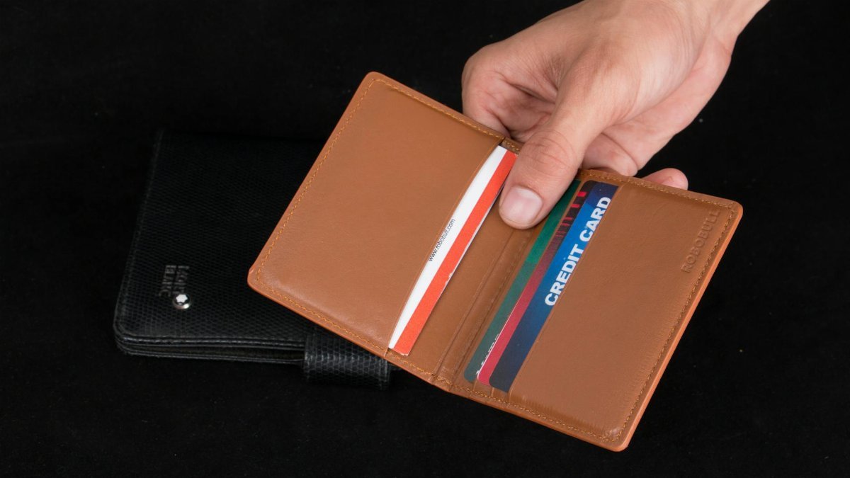 Close-up of a hand holding an open brown leather wallet filled with credit cards.