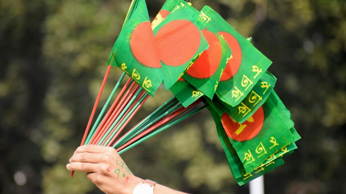 Close-up of a hand holding multiple Bangladesh flags during Victory Day celebrations.