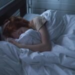 A woman sleeping peacefully in a cozy bedroom, enveloped by soft white sheets, under the gentle glow of night lighting.