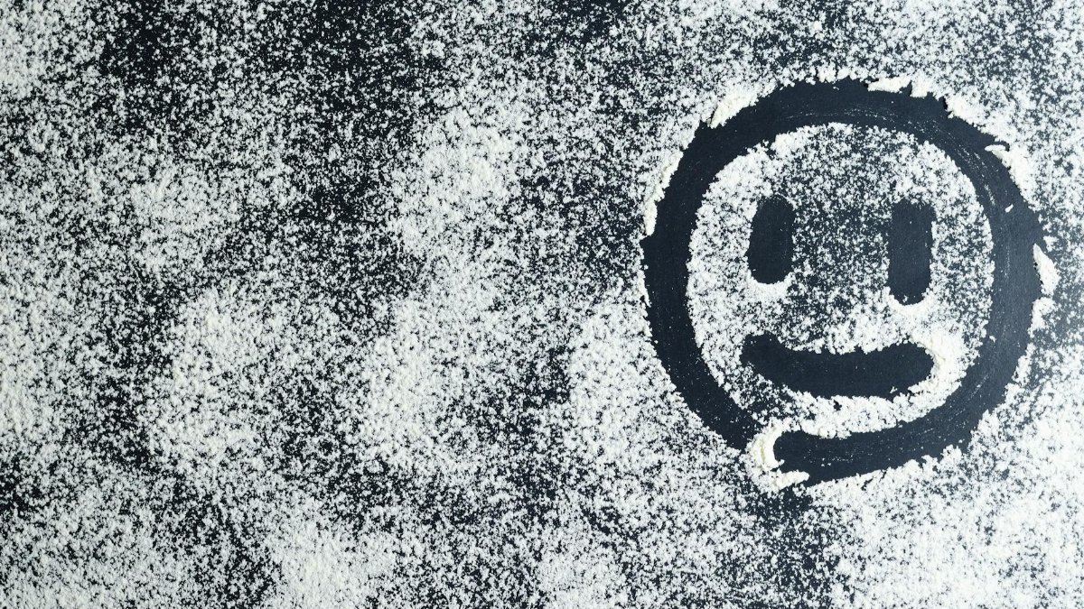 Artistic smiley face drawn through white powder on a black surface, creating an abstract texture.