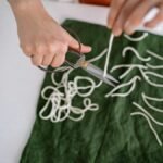 Close-up of hands cutting candle wicks on green fabric, showcasing craft skills.