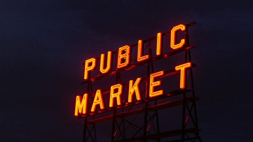 Illuminated 'Public Market' neon sign glowing against a twilight sky.