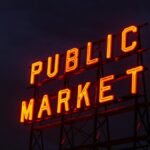 Illuminated 'Public Market' neon sign glowing against a twilight sky.
