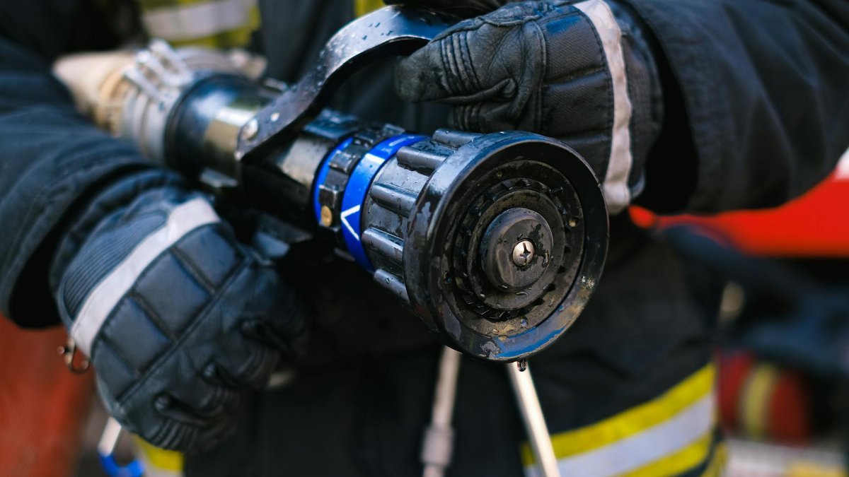 Detailed close-up of a firefighter in gear holding a water hose nozzle, emphasizing safety and emergency readiness.
