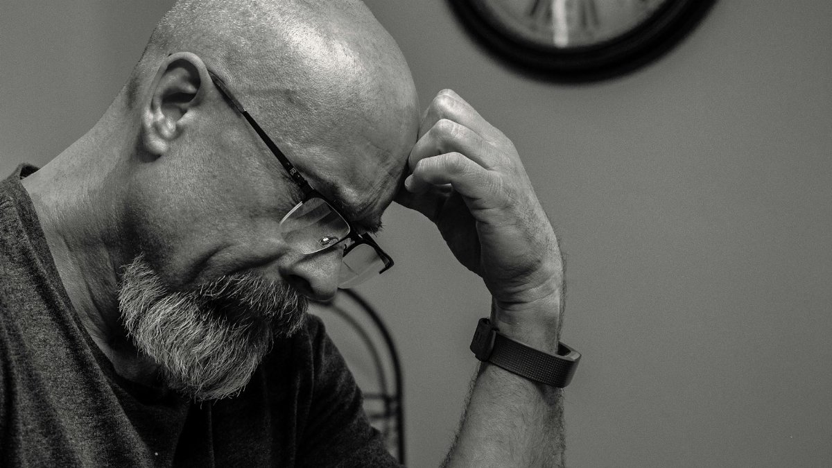 Black and white portrait of a thoughtful bald man indoors, capturing a moment of reflection with a wall clock in the background.