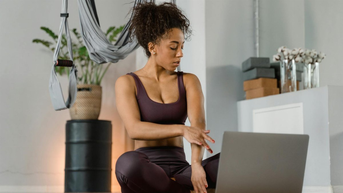 A woman in yoga attire uses a laptop for meditation in an indoor setting, promoting digital wellness.