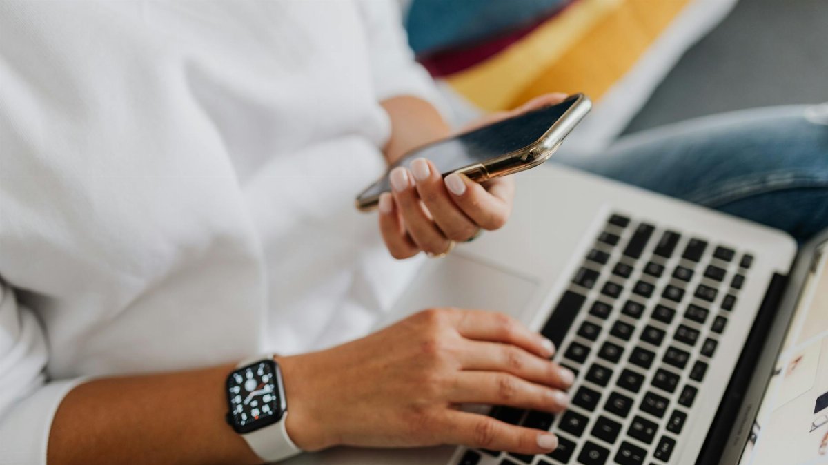 Close-up of a person using a smartphone and laptop for work, showcasing multitasking in a modern home office setting.