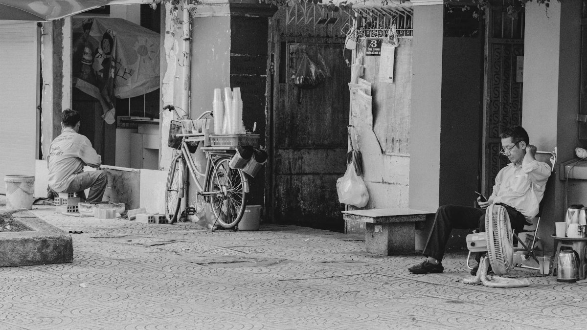 Two men sit and work on a quiet street, capturing daily life in an urban setting.