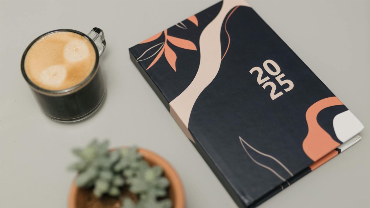 A modern 2025 planner next to a cup of coffee and a potted succulent on a neutral background.