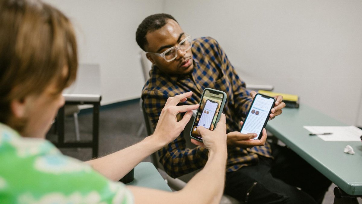 Two students collaborate, exchanging information on smartphones during a classroom session.