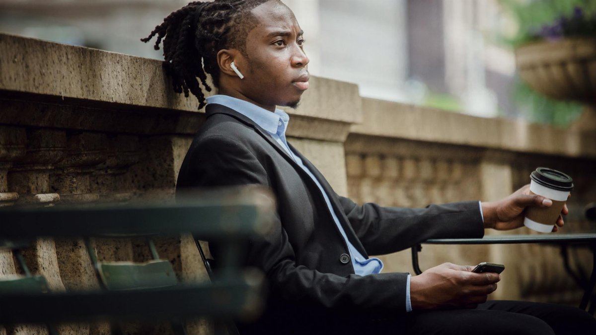 A young professional man in a suit enjoys coffee while listening to music outdoors.