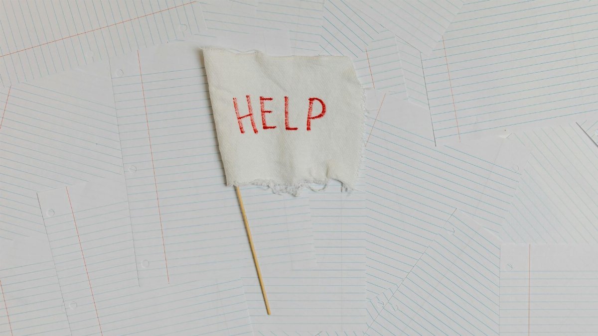 A fabric flag with 'HELP' on a scattered notepaper background, symbolizing distress or overwhelm.