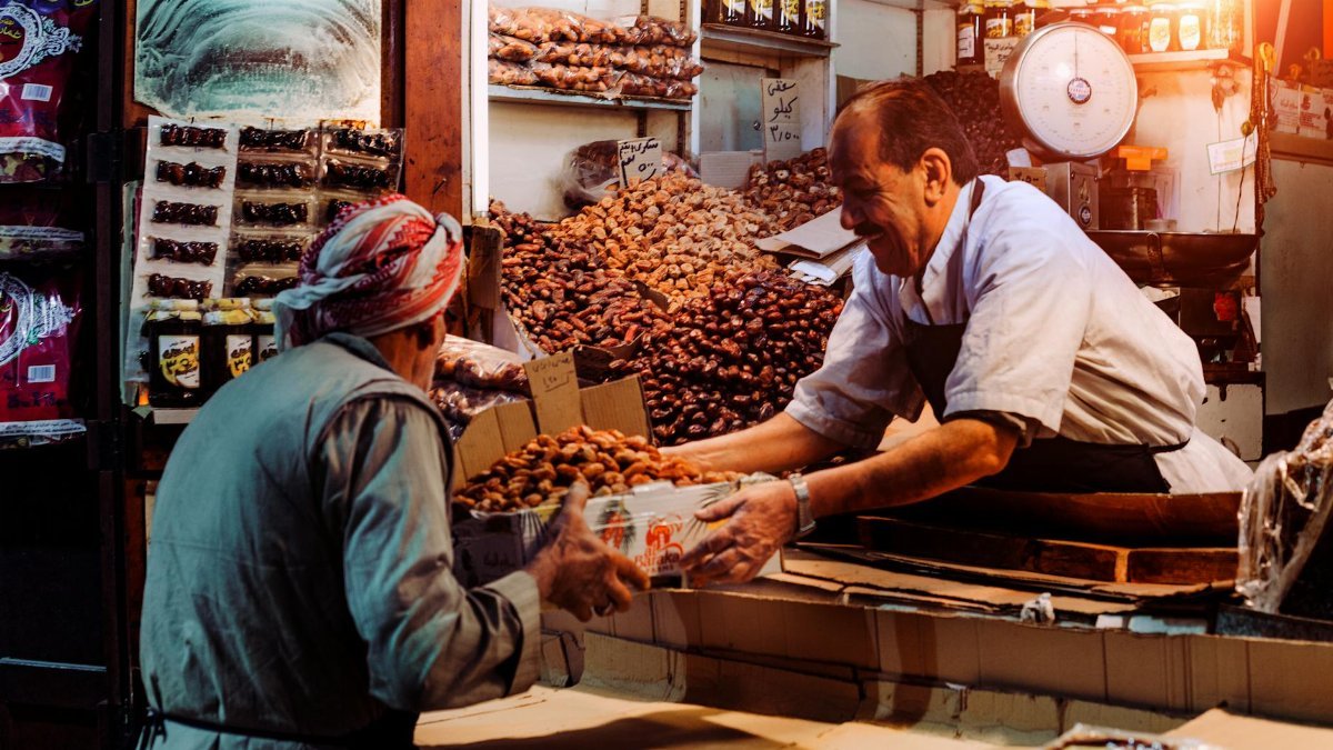 Two men exchanging dates in a vibrant Dubai spice market stall.