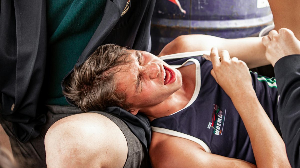 A young male athlete grimacing in pain due to muscle cramps during a sports event.
