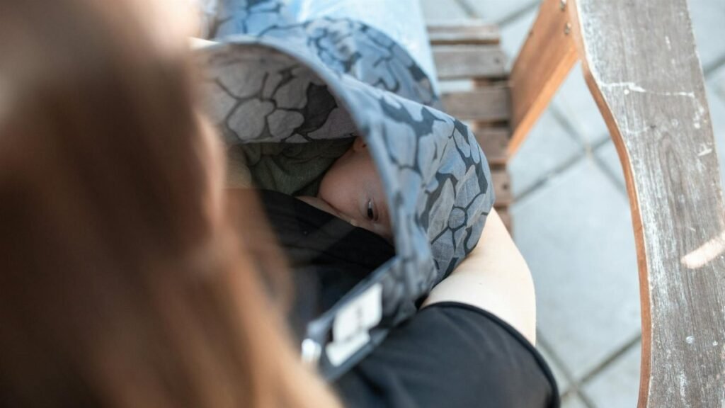 Intimate outdoor moment of mother breastfeeding baby under cover on a bench.