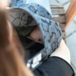 Intimate outdoor moment of mother breastfeeding baby under cover on a bench.