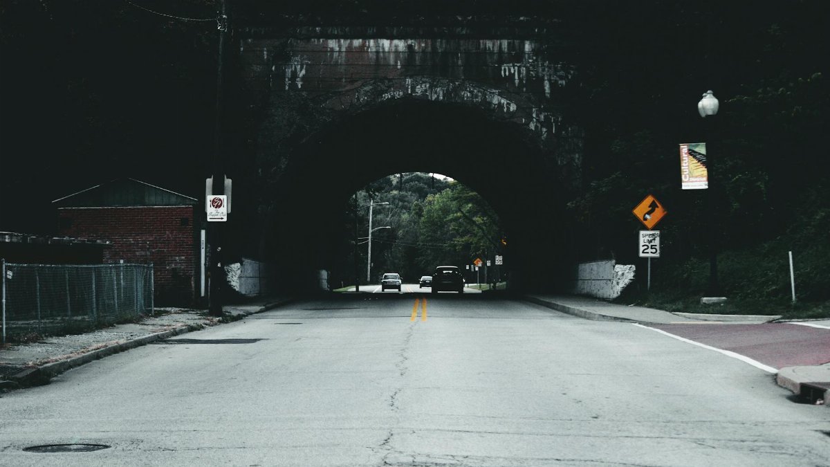 A quiet urban road leading through a tunnel with visible traffic and speed signs.