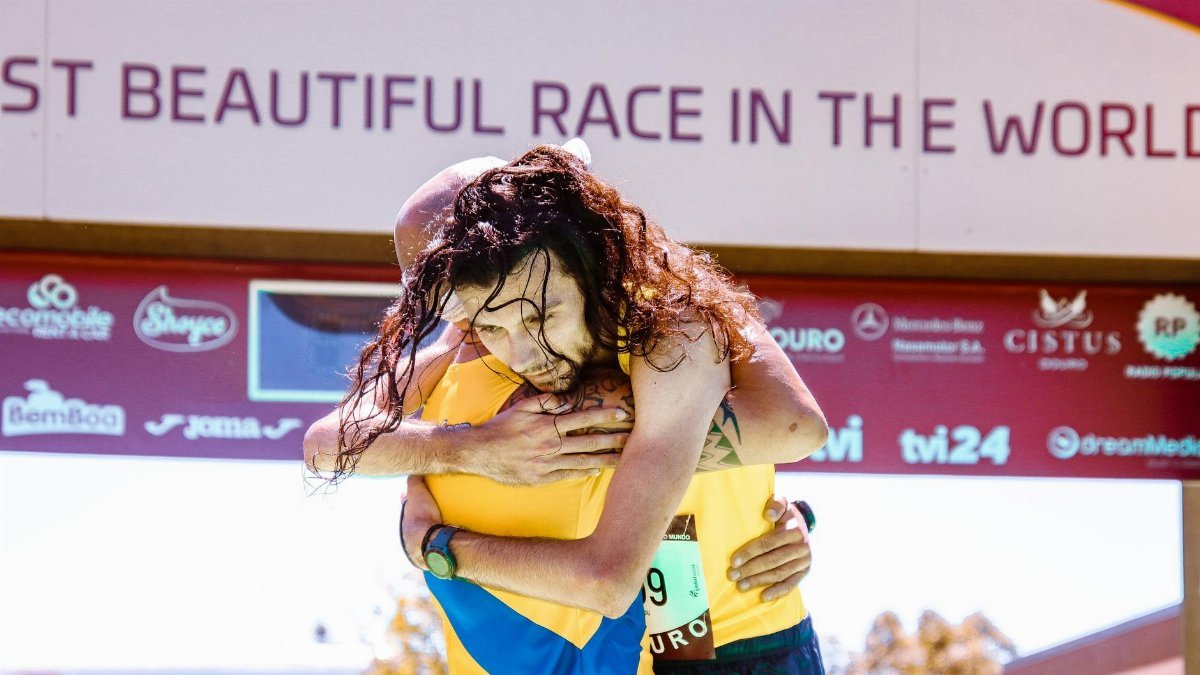 Two runners share an emotional hug at a race finish line.
