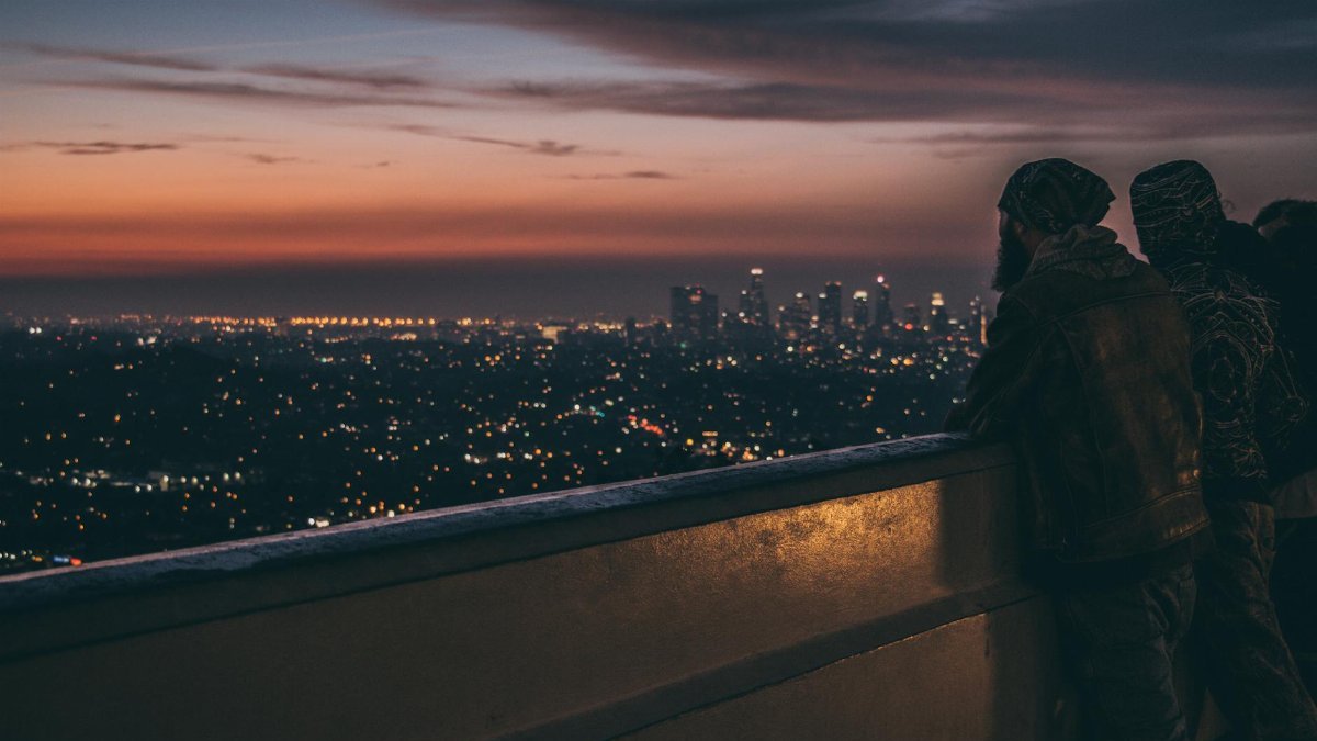 View of a city skyline at twilight from a balcony, with people silhouetted against the sunset.