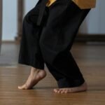Person practicing martial arts barefoot on a wooden floor indoors.