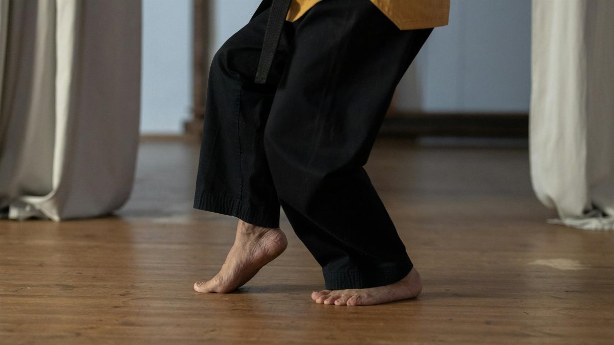 Person practicing martial arts barefoot on a wooden floor indoors.
