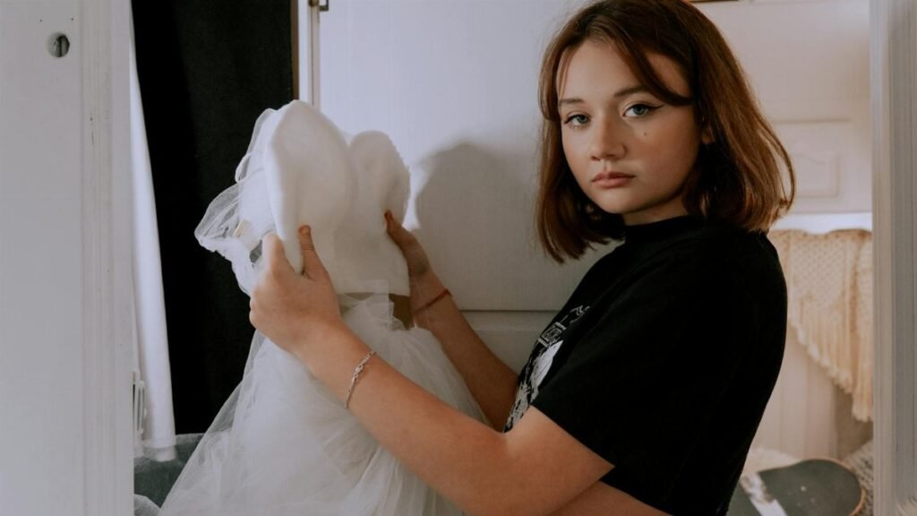 Teen girl holding a wedding dress indoors, conveying contemplation and future planning.